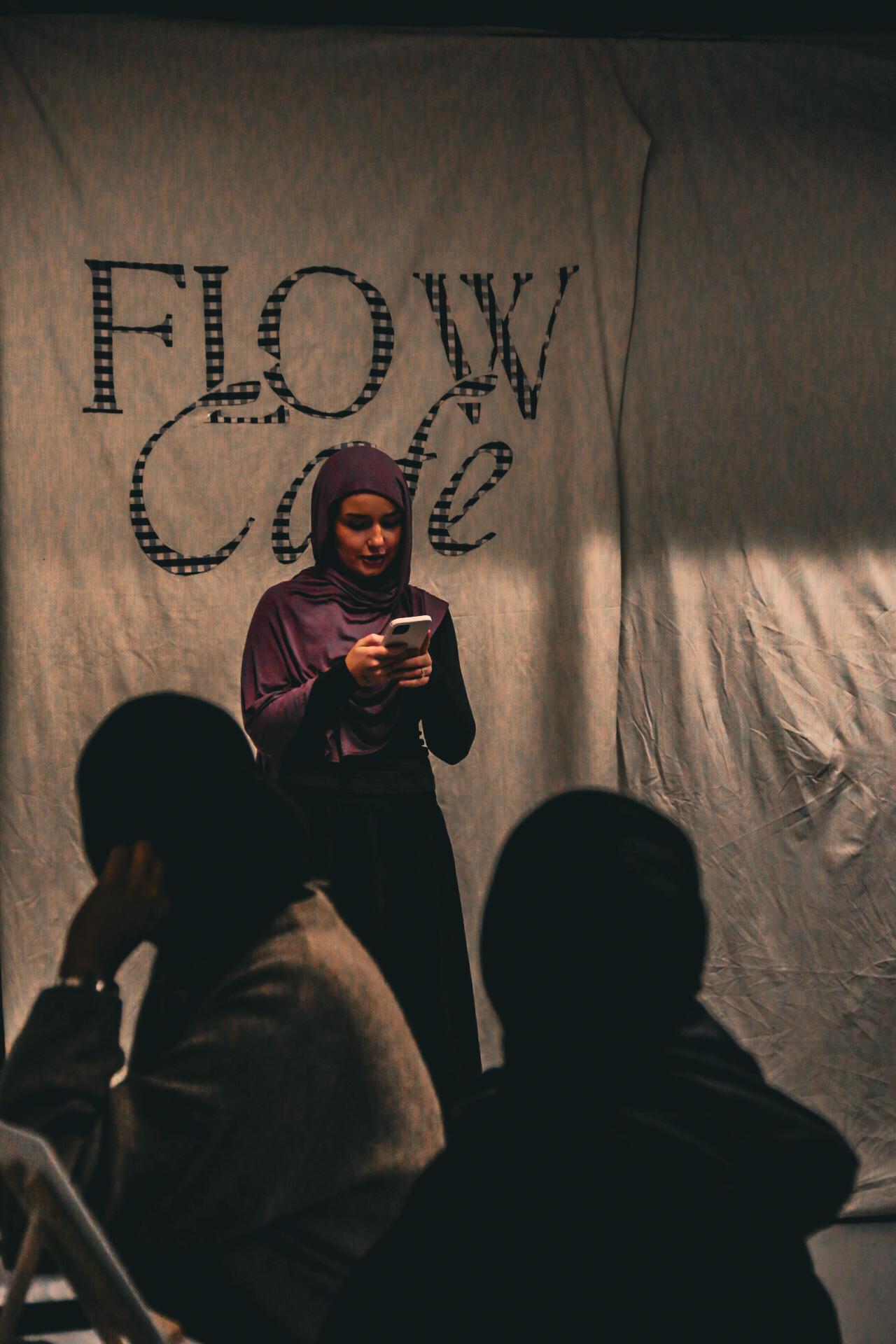 A woman speaking in front of a handmade Flow Café backdrop
