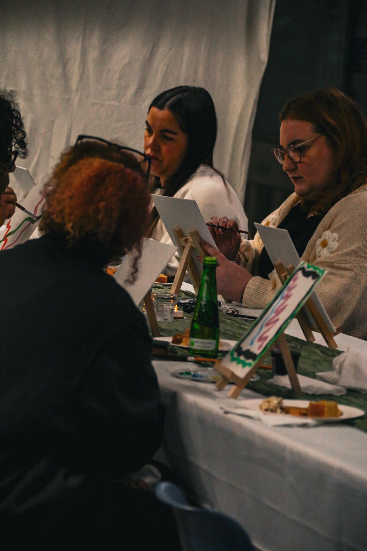 Women painting individual canvases around a shared table