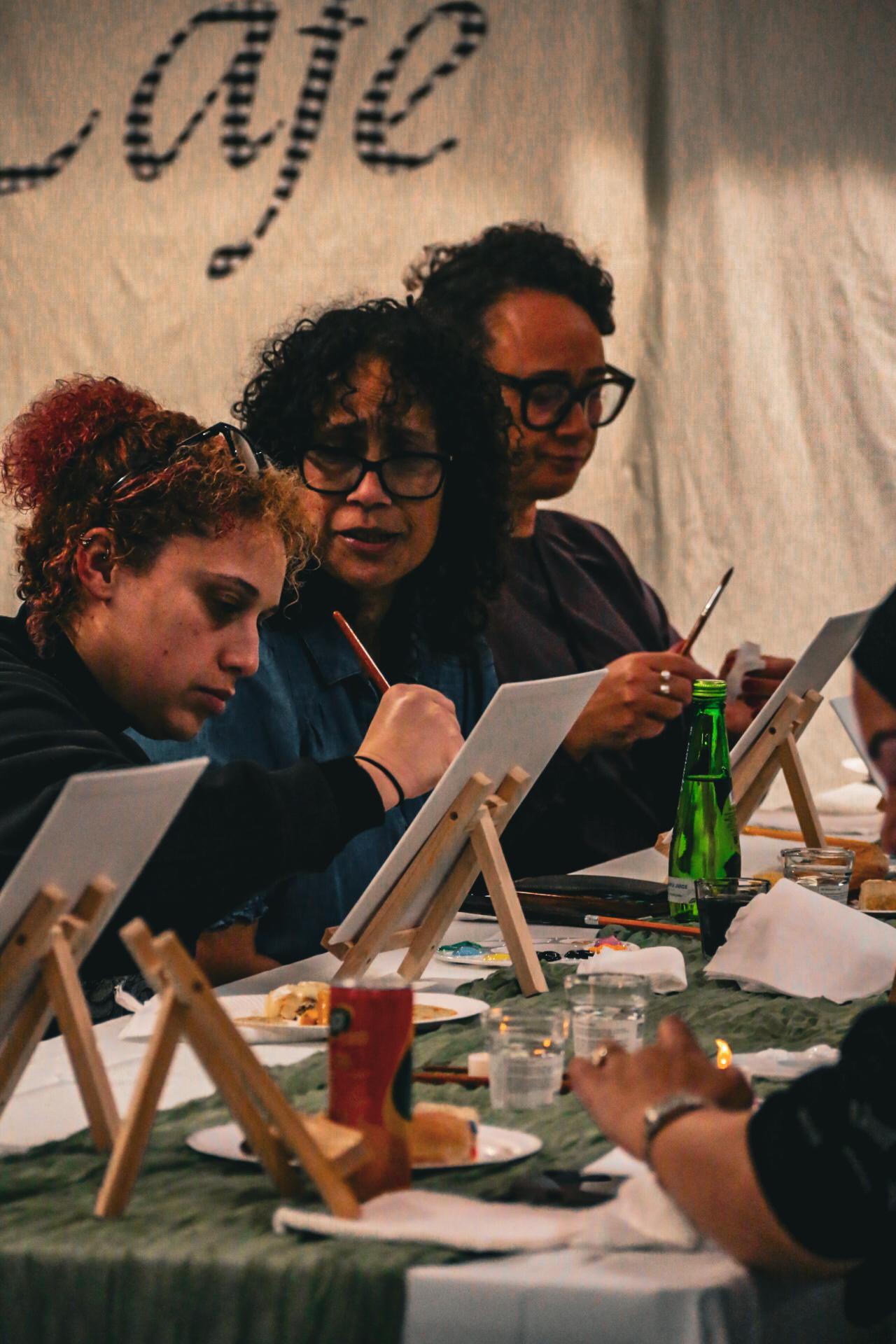Women concentrating as they paint small canvases together